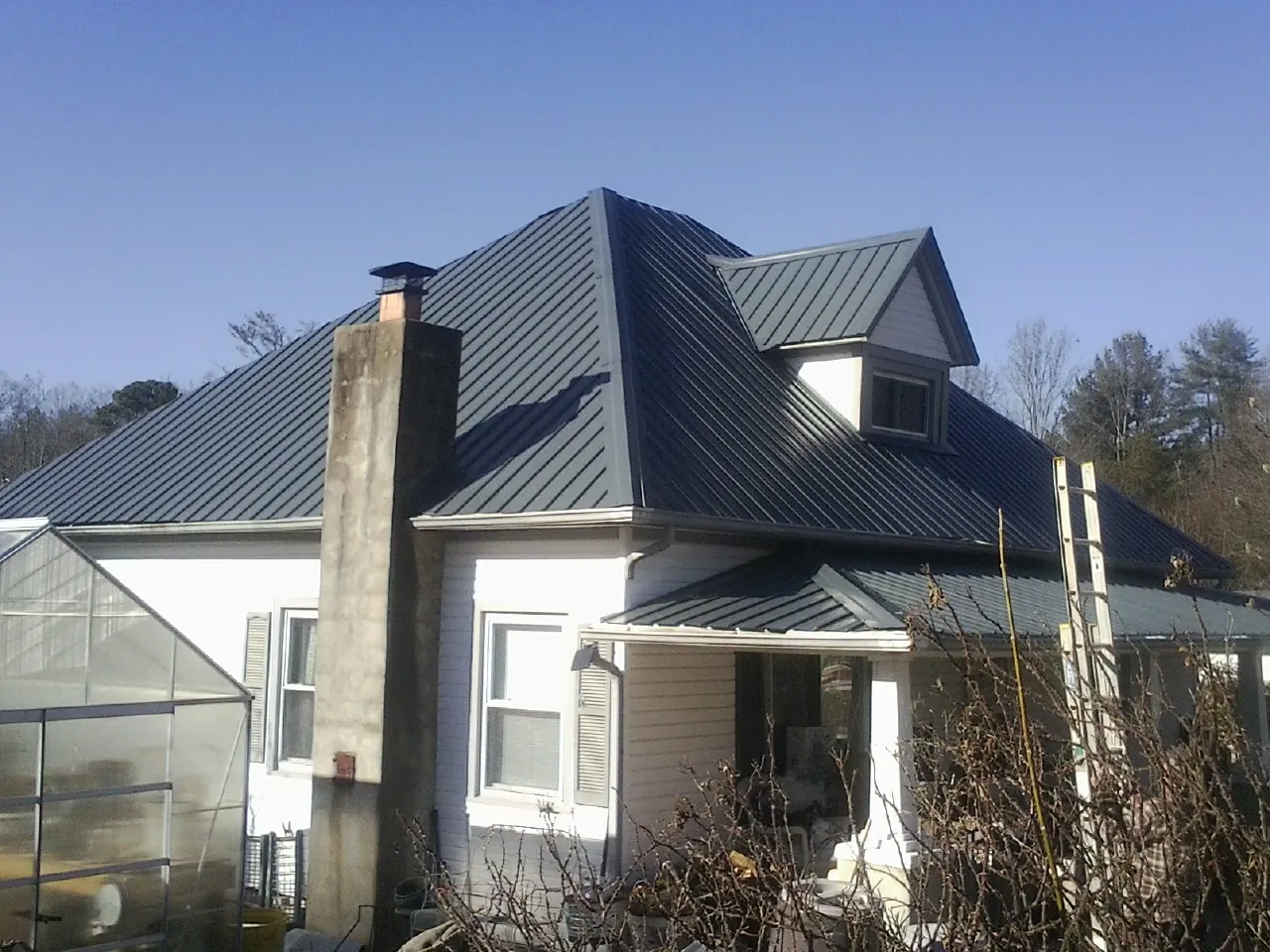 Dark blue standing seam metal roof on a white farmhouse with dormer — Slate & Tile Roof Repair by Roofing Brothers in Dairy