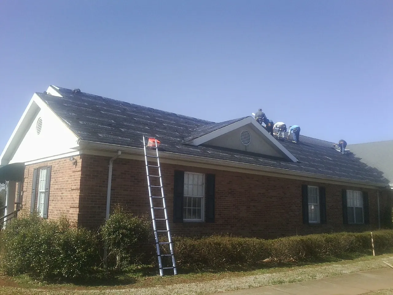 Crew tearing shingles off a brick ranch roof with a ladder set — Metal Roof Repair work by our crew in Dairy