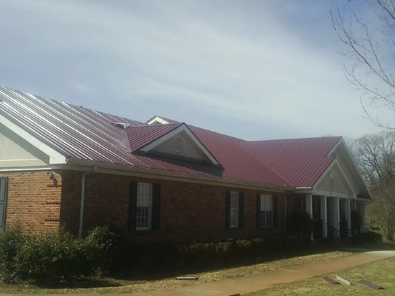 Red metal roof with gabled entries on a long brick building, from a Hail Damage Roof Repair job in Dairy