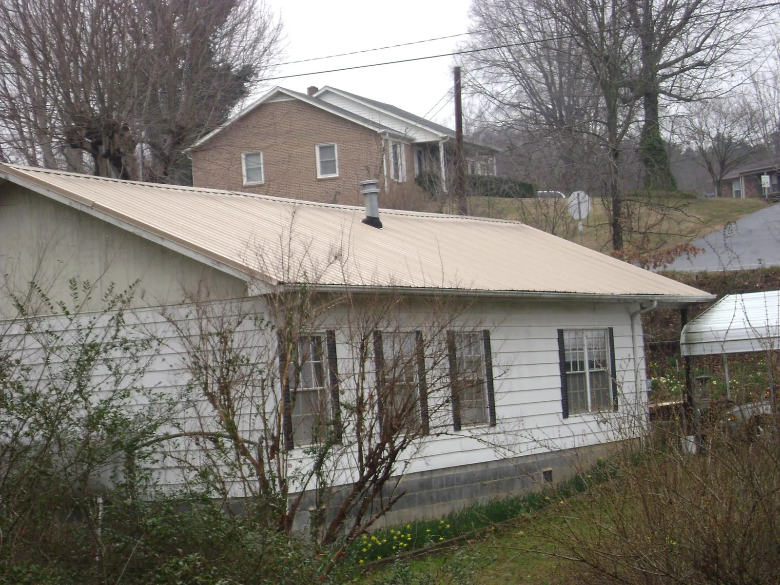 Tan metal roof on a white sided house set into a hillside — Commercial Roofing by Roofing Brothers in Dairy